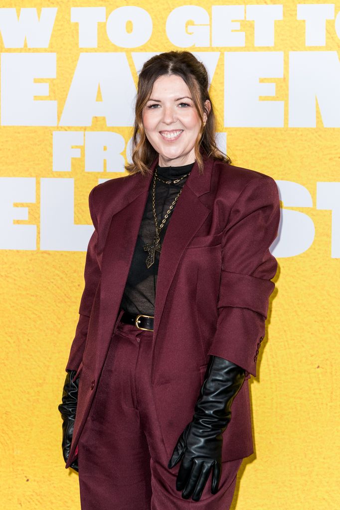 Lisa McGee pose avec un sourire, vêtue d'un costume marron assorti et de gants en cuir.