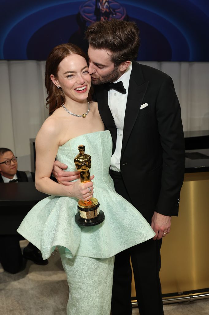 Emma stone in a mint green dress holding oscar smiling next to partner Dave mccary