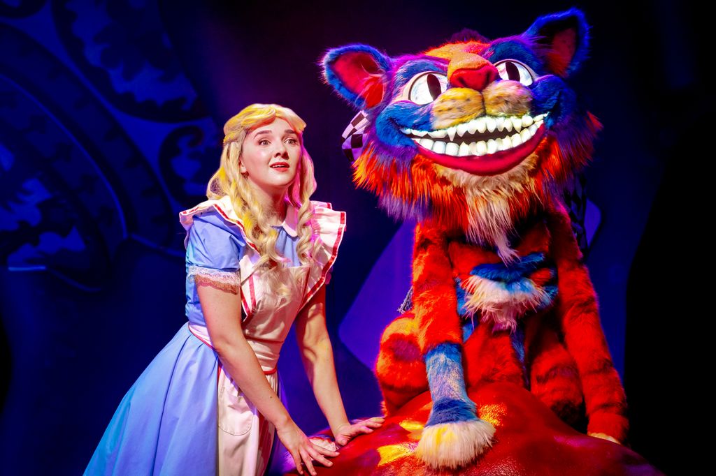 Girl dressed up as Alice in Wonderland next to a huge puppet of the Cheshire Cat
