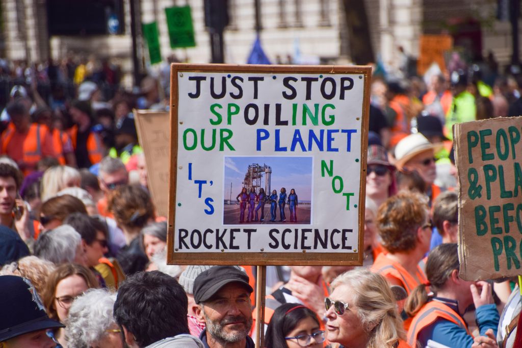 A protester holds a 'Just stop spoiling our planet' placard with a picture of Katy Perry and other women who took part in the Blue Origin space flight, as Just Stop Oil activists pass through Parliament Square during their final protest