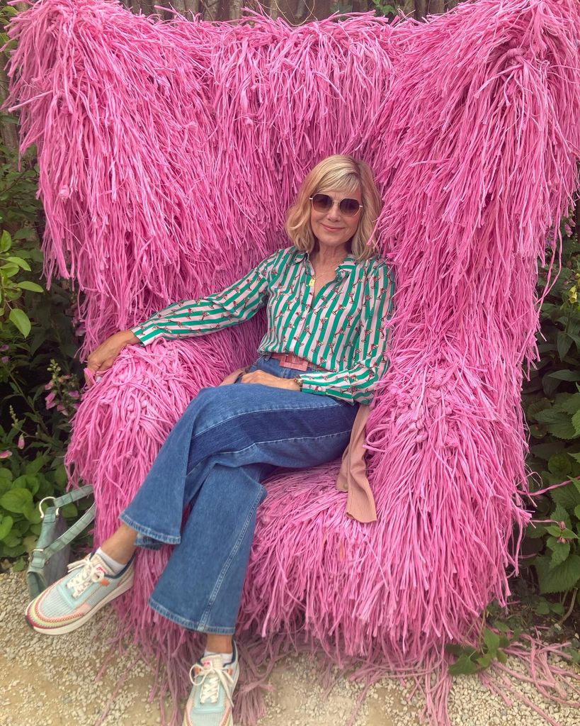 Glynis Barber está sentado en un asiento rosa rosa en jeans y una camisa pegajosa