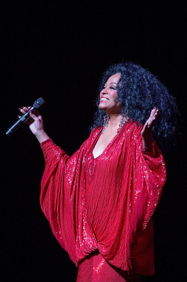 Diana Ross dans une robe rouge brillante tenant un microphone, souriant et tenant ses bras