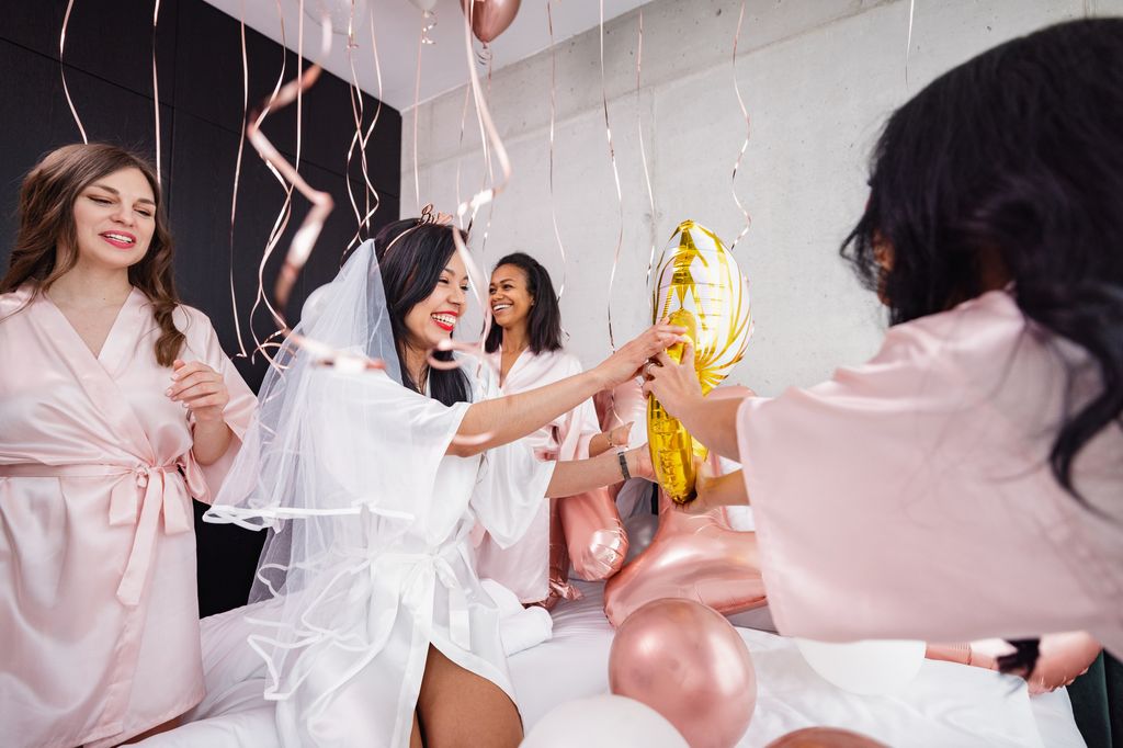bride-to-be and her friends having fun and smiling while playing with the balloon decorations in the bedroom.