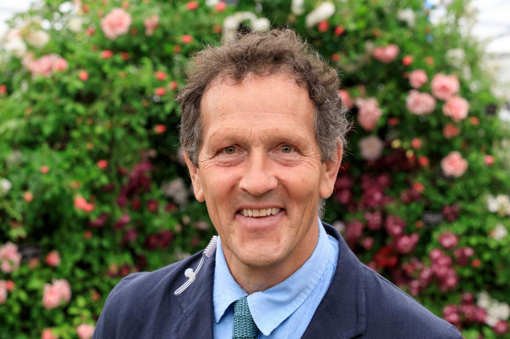 Monty Don smiling in a suit in front of a floral wall