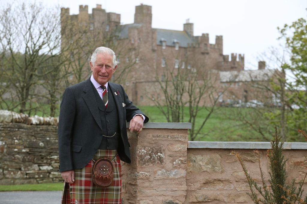 king charles posing in tartan in front of Scottish castle