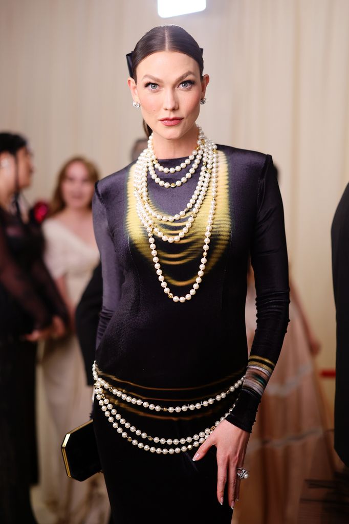 Karlie Kloss wears a black and yellow Loewe gown at the Met Gala, styled with layered pearl necklaces and pearl belt channeling Karl Lagerfeld-inspired elegance.