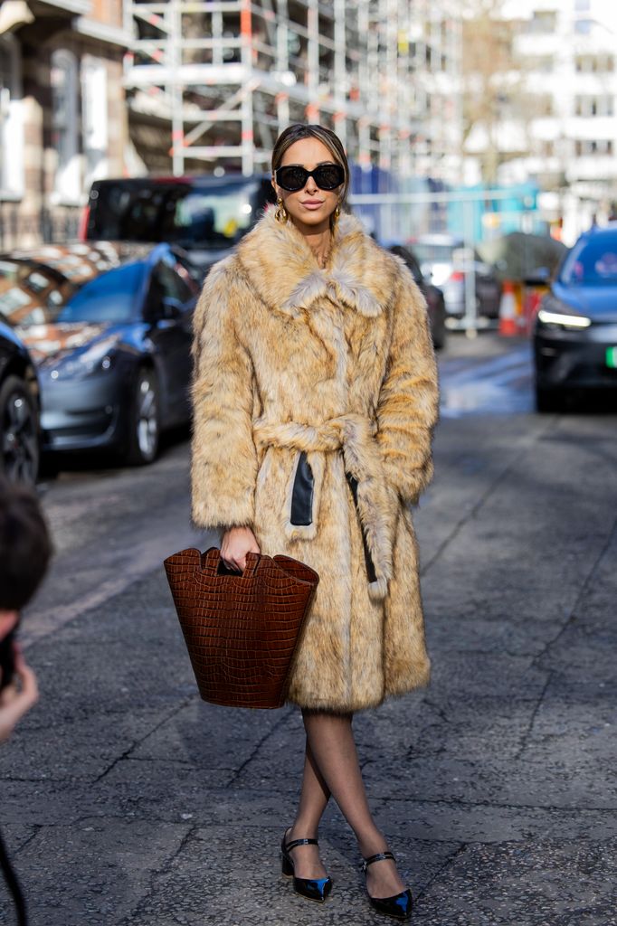Isabella Charlotta Poppius wears belted beige fur coat, brown bag, tights, pointed shoes, sunglasses outside Bora Aksu during London Fashion Week February 2024 on February 16, 2024 in London, England