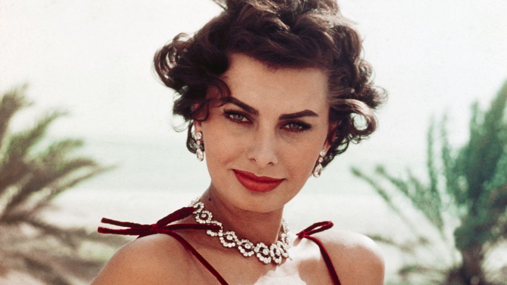 Sophia Loren posing outdoors in a red spaghetti strap dress and a diamond necklace 