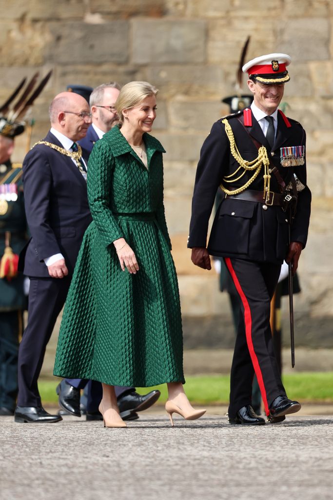 Sophie in green look walking with uniformed man 