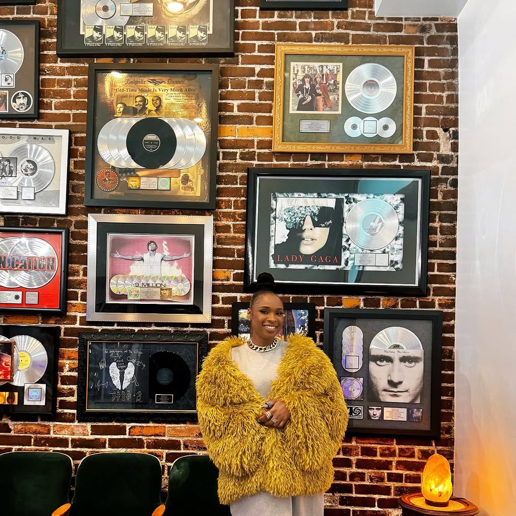 jennifer hudson poses in front of a brick wall covered in records