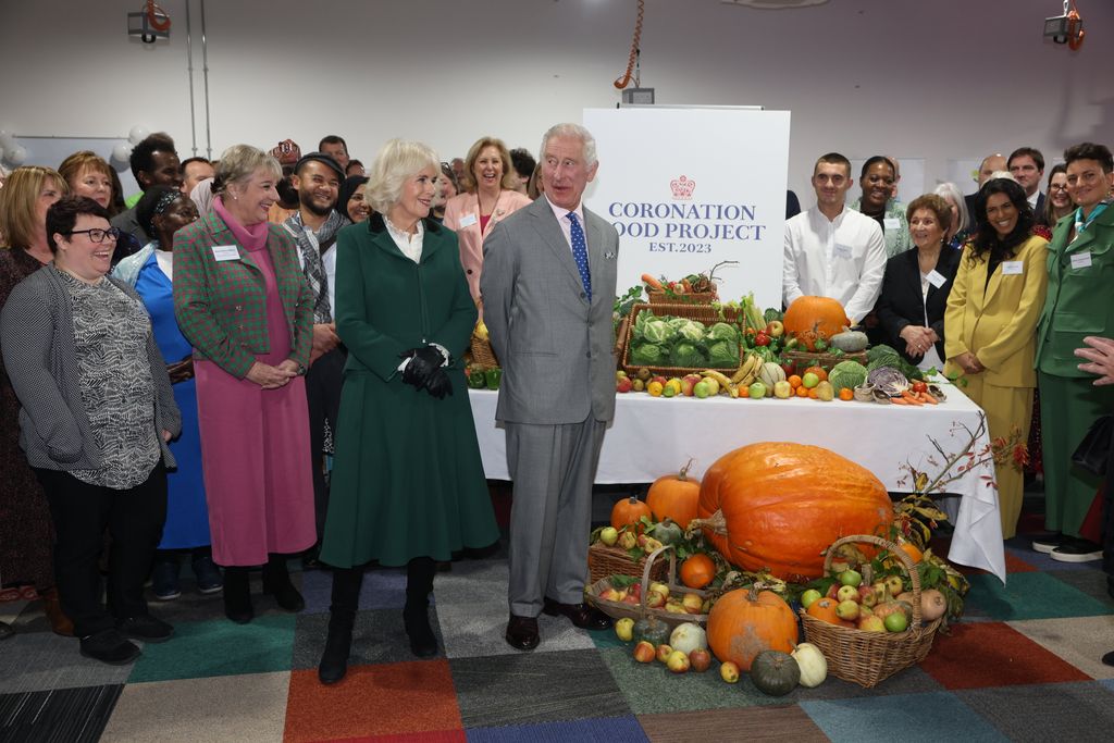 King Charles and Queen Camilla standing with staff and local produce at the Coronation Food Project