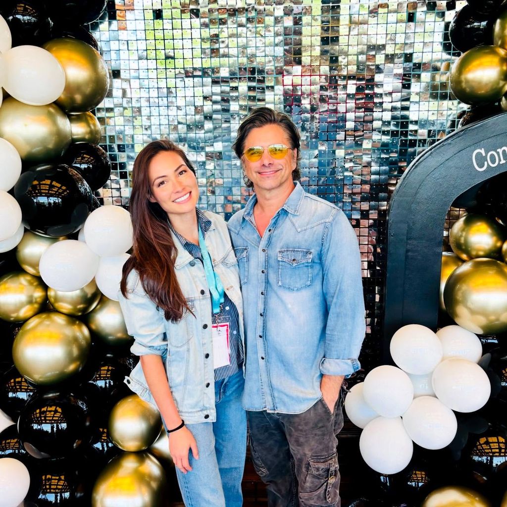 john stamos and wife caitlin posing in front of balloon arch