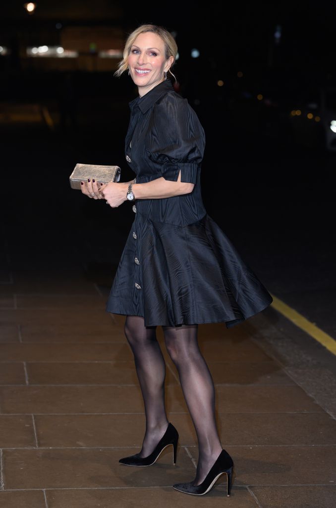 Zara Tindall smiling while holding a clutch bag in a black mini dress