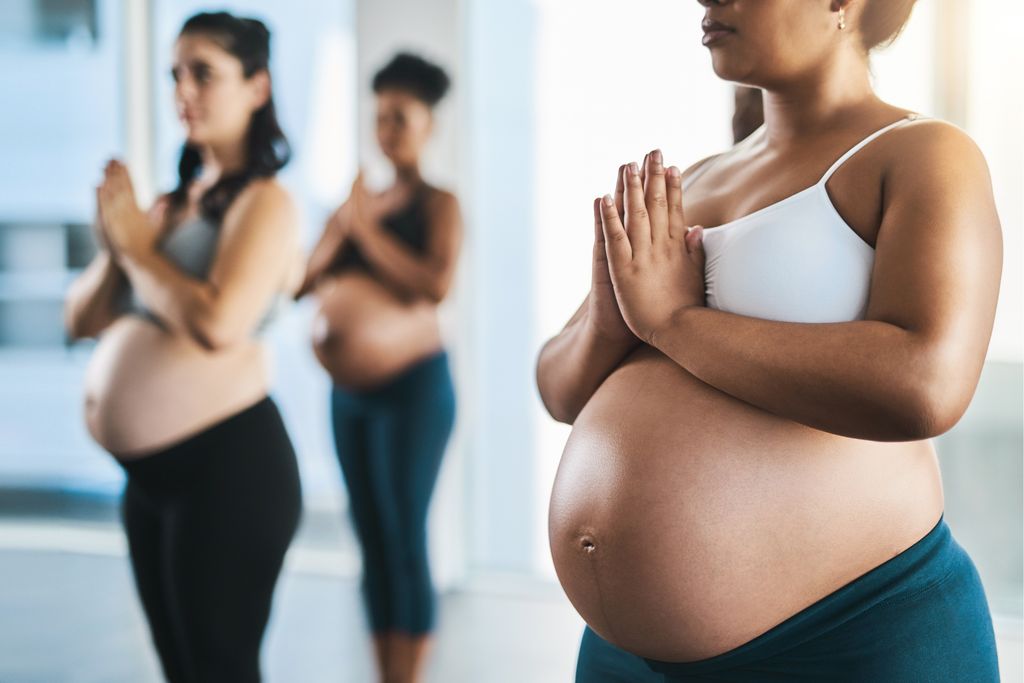 a group of young pregnant women meditating and practising yoga together in studio