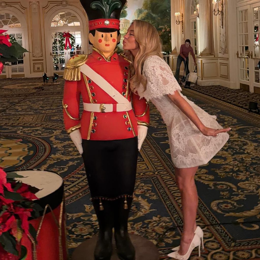 Sydney Sweeney kisses a lifesize Nutcracker statue, wearing a white lace mini dress and matching heels 