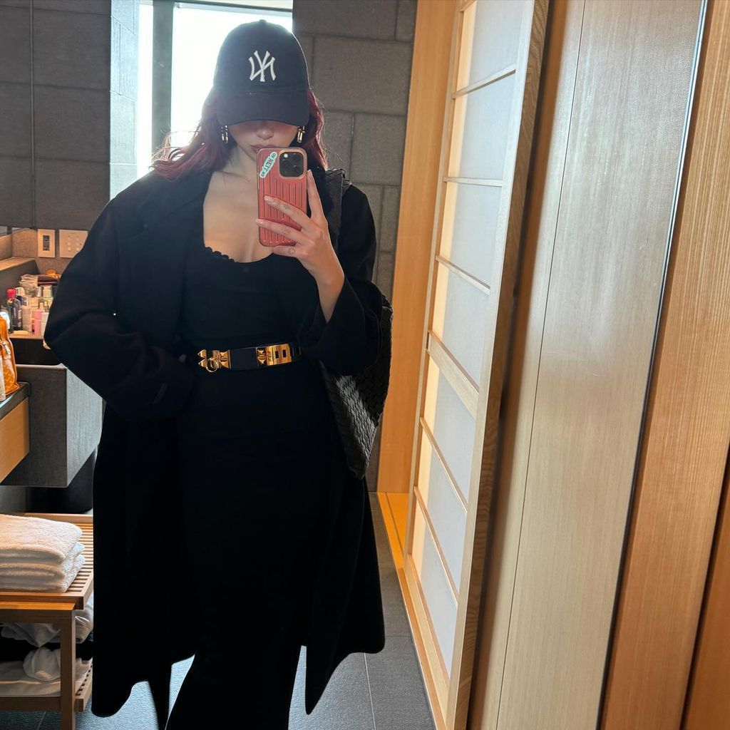 Dua in black bodysuit, coat, cap