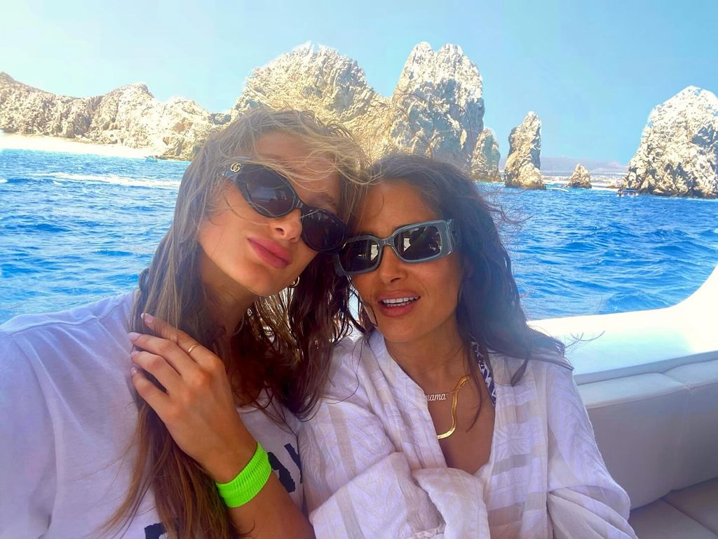 salma hayek and stepdaughter mathilde sitting on a boat wearing sunglasses with the sea behind them