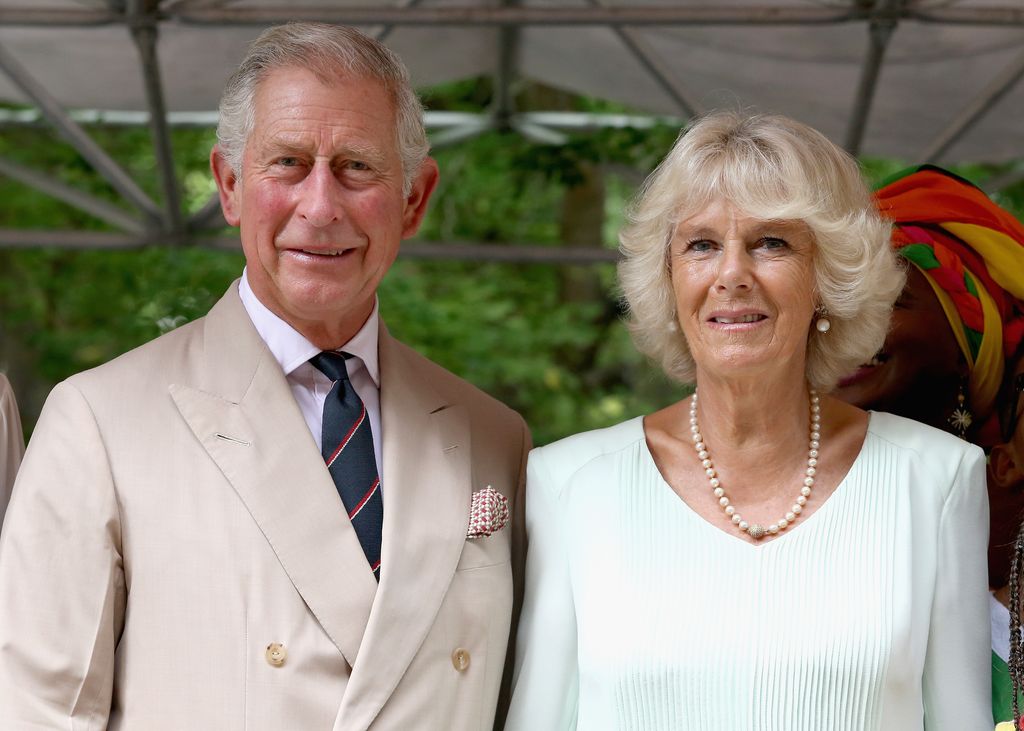 King Charles and Camilla looking serious in light coloured clothing