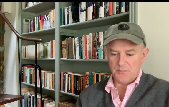 Hugh sat in front of bookcase at home