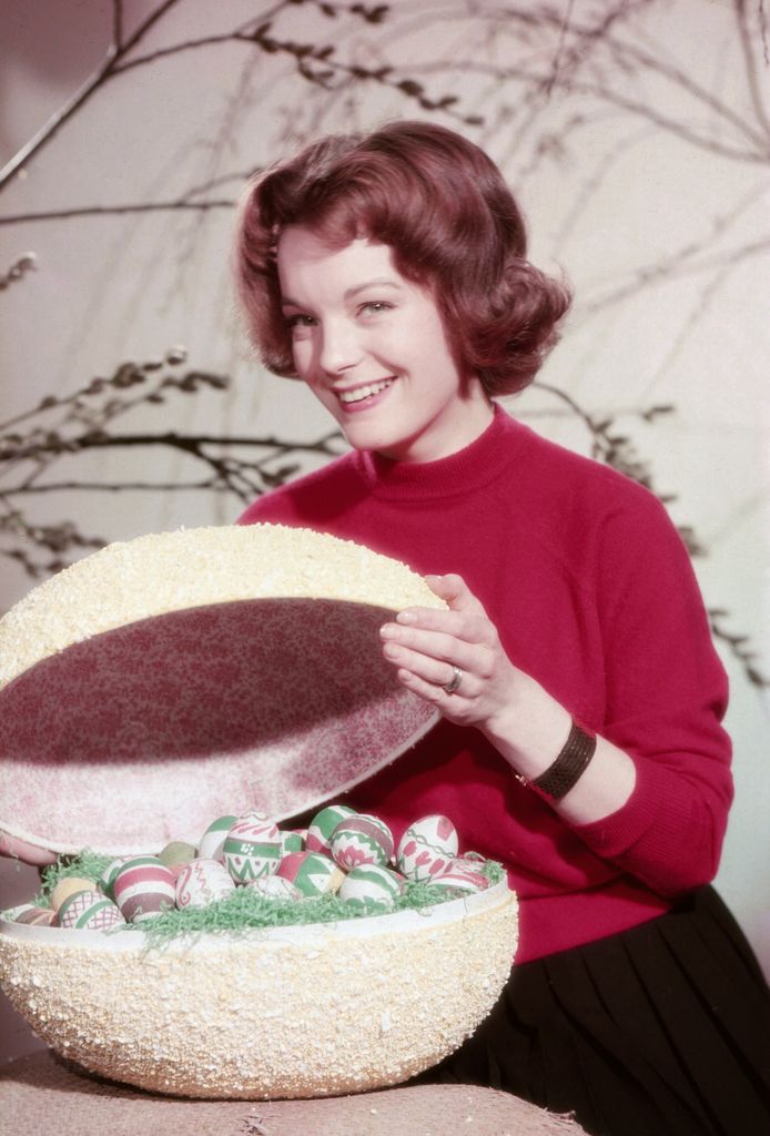 Romy Schneider in a red sweater holds a giant egg full of colorful Easter eggs.