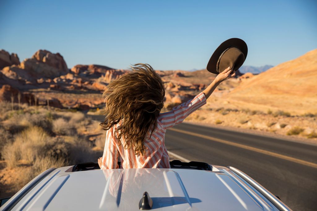 A woman celebrating out her sunroof window in the desert.