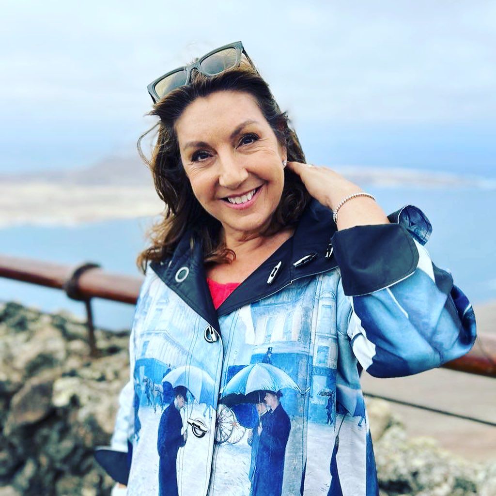 Jane McDonald wearing a blue coat and smiling by the beach