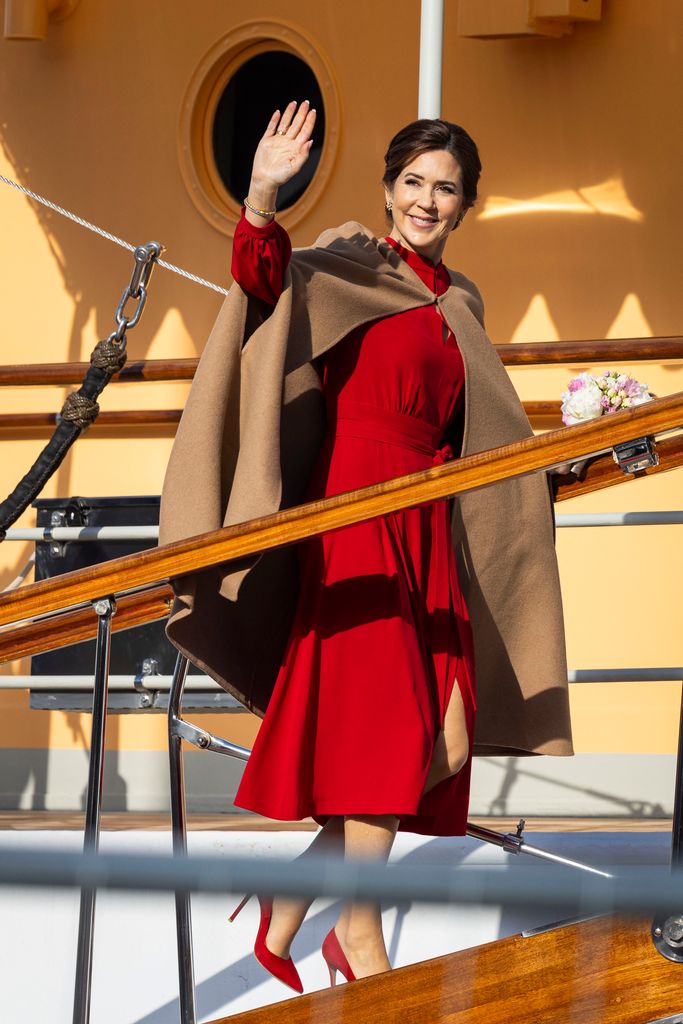Queen Mary waving boarding boat in red dress
