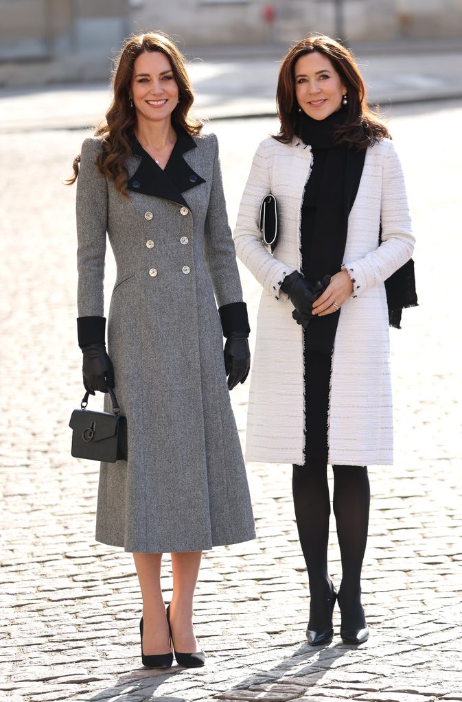 Kate Middleton standing alongside Mary, Crown Princess of Denmark wearing a grey double breasted coat and a black top handle bag 