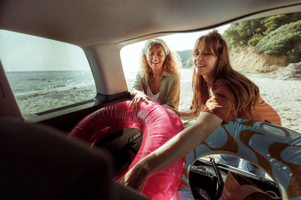 Two female friends unpacking car trunk at the beach