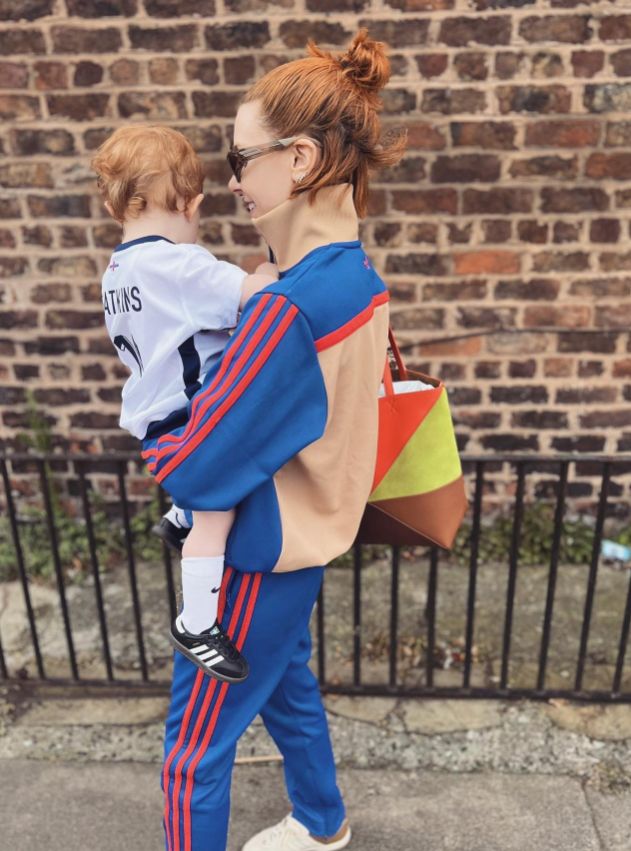 Stacey Dooley in a tracksuit carrying a young girl in a football kit