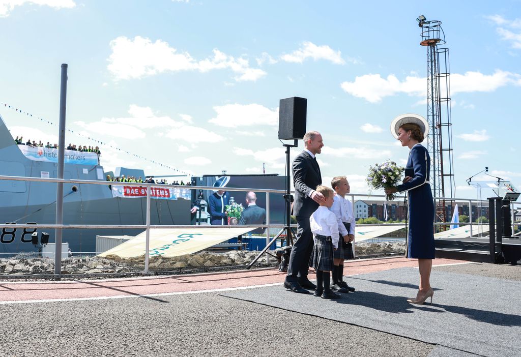 Kate Middleton in navy and white dress speaks to two little boys