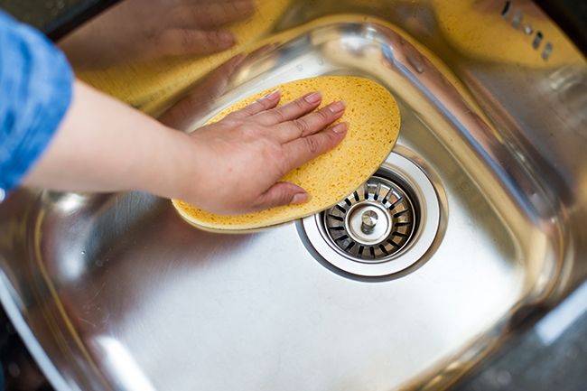 A person cleaning a stainless steel kitchen sink