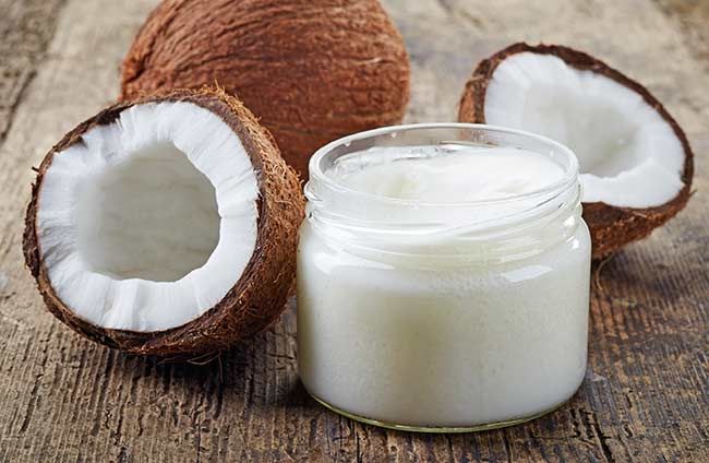 a jar of coconut oil next to two halves of an open coconut on a wooden table