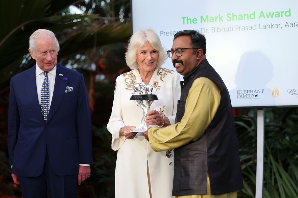 Queen Camilla handing over an award with King Charles standing by her