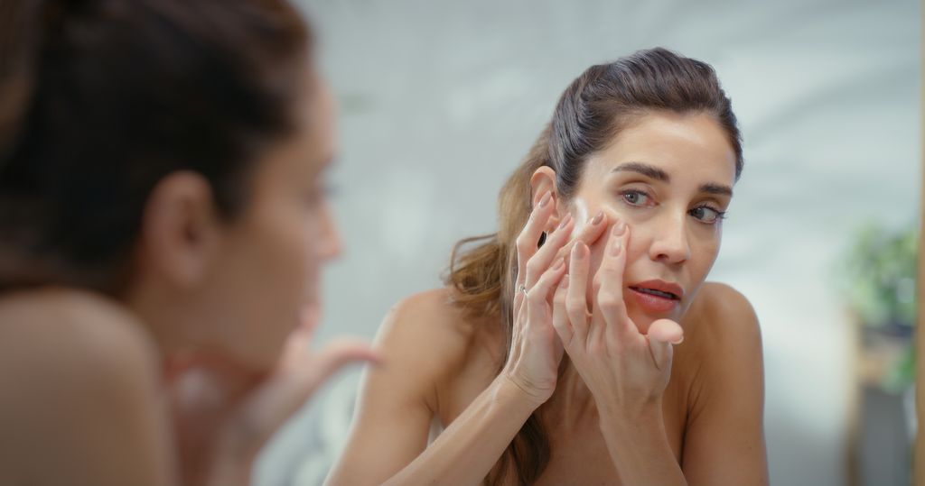 Mature woman, mirror and pimple with skincare in home, acne or reflection with routine in morning