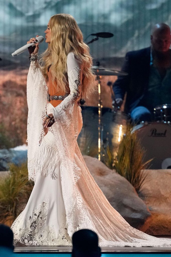 Carrie Underwood side on singing in white maxi dress