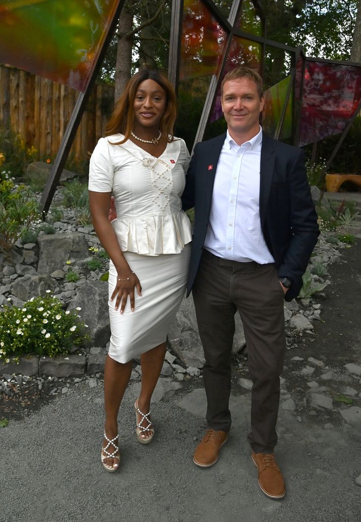 DJ Cuppy in a ruched ivory dress with pearls and Joe Perkins in a blazer pose at Chelsea Flower Show.