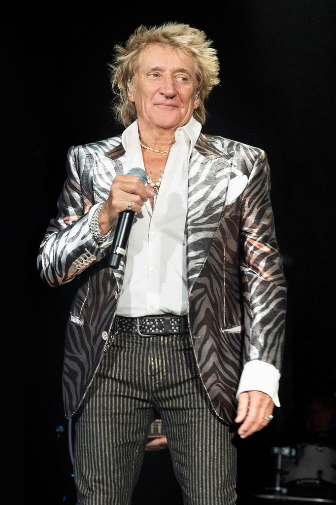 Rod Stewart in a zebra striped blazer, white shirt and striped pants holding a microphone 