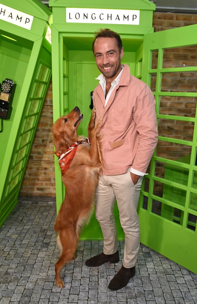 James middleton wearing a pink jacket and beige trousers while standing outside a neon green phone box 