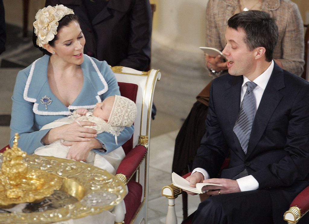 Queen Mary holding Prince Christian while King Frederik sings to him during a christening