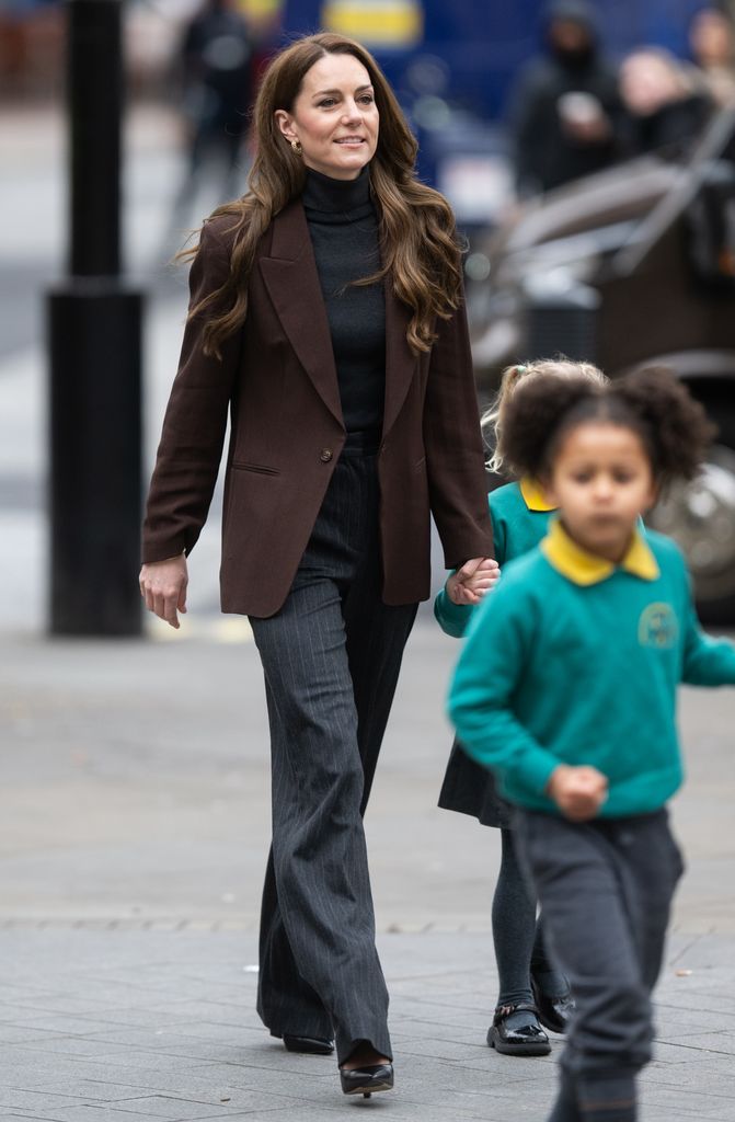 Catherine, Princess of Wales holding hand of school child in brown blazer