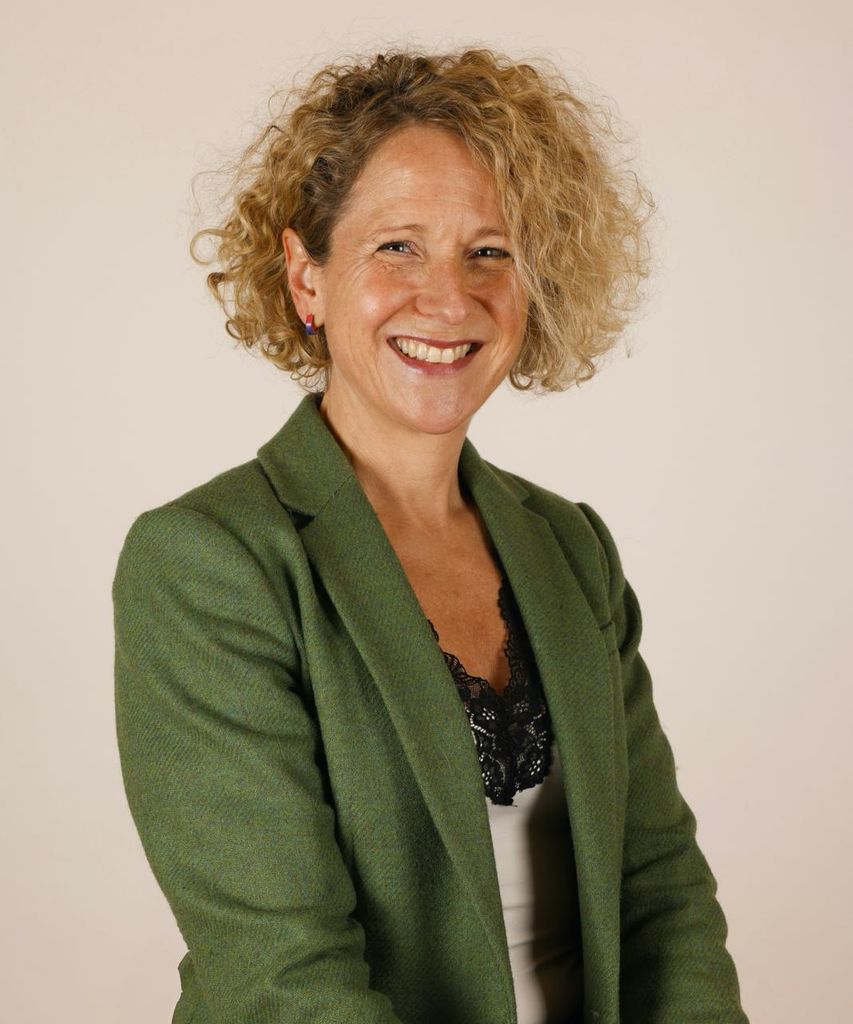 Femme de la quarantaine aux cheveux blonds bouclés souriant dans un blazer vert
