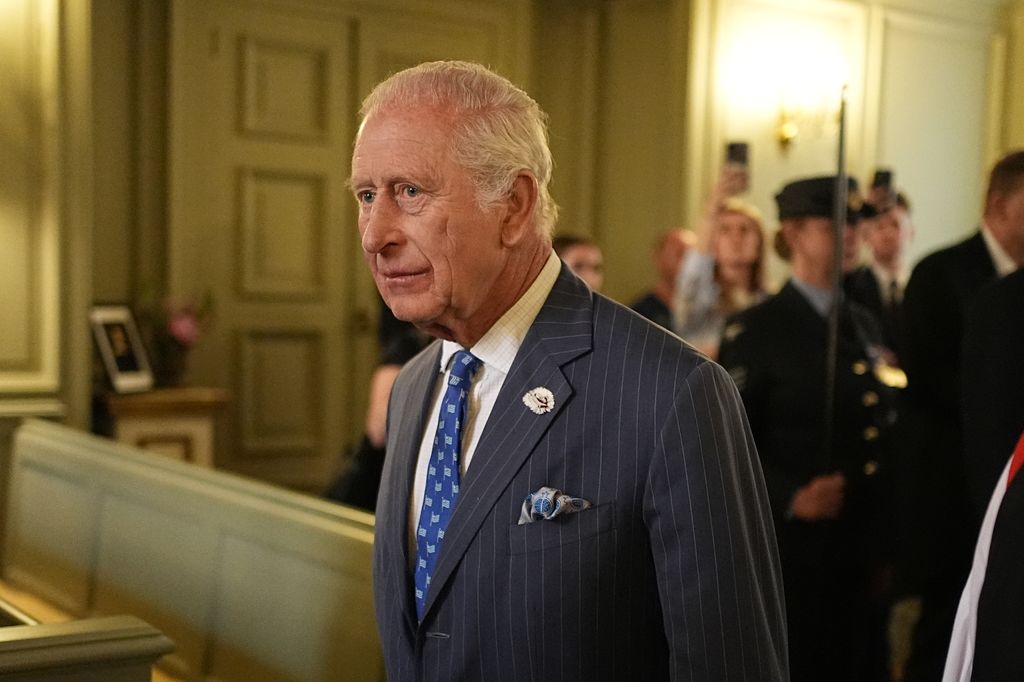 King Charles walking through a building with a sullen expression on his face