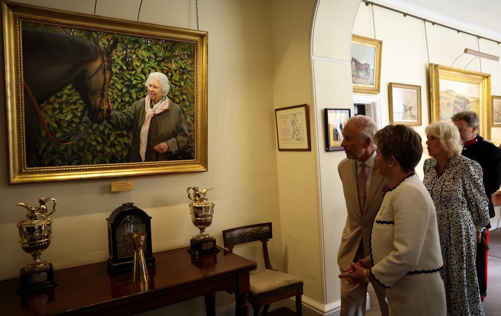 King Charles III (rear L) and Queen Camilla (R) look at a painting portraying late Queen Elizabeth II during a visit with Senior Steward of The Jockey Club