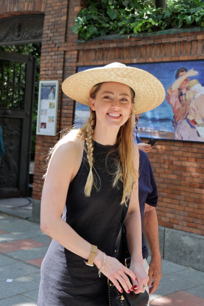Amber Heard smiling in a sun hat on a sunny street in Madrid
