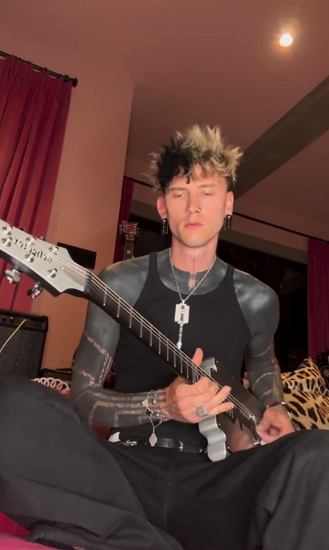 Machine Gun Kelly playing guitar in his home