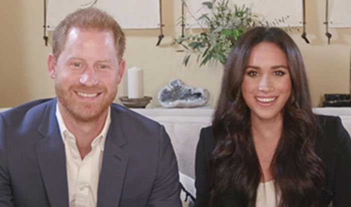 prince harry and meghan smiling at camera on sofa 
