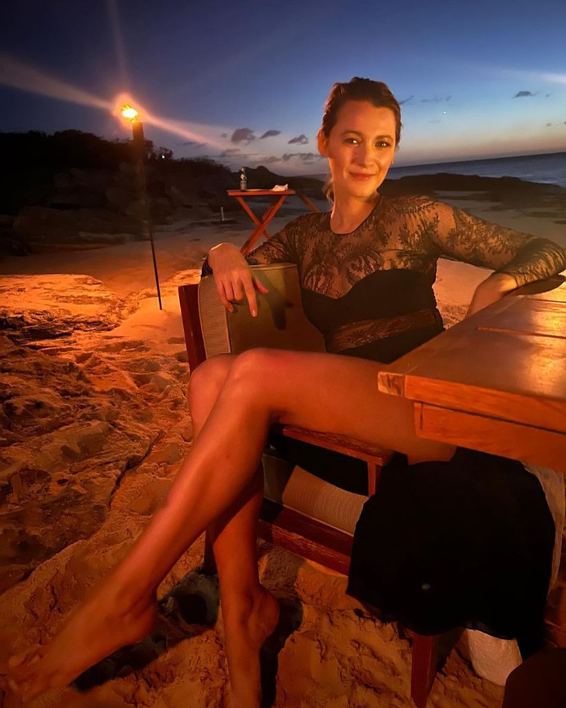 Blake Lively sits on a wooden chair sideways on the beach