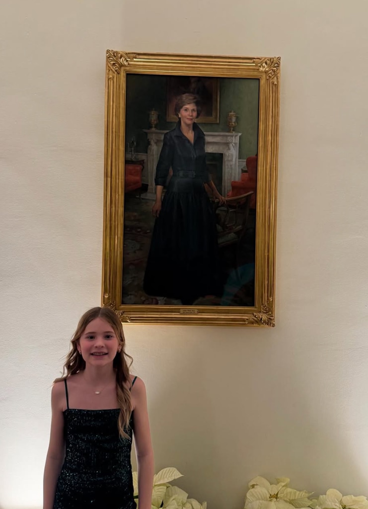 Photo shared by Jenna Bush Hager from attending a White House Christmas party, featuring her daughter Mila posing with a portrait of her grandmother Laura Bush