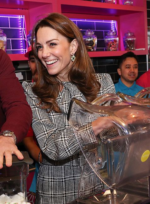 kate wearing a check blazer laughs with someone in a busy kitchen